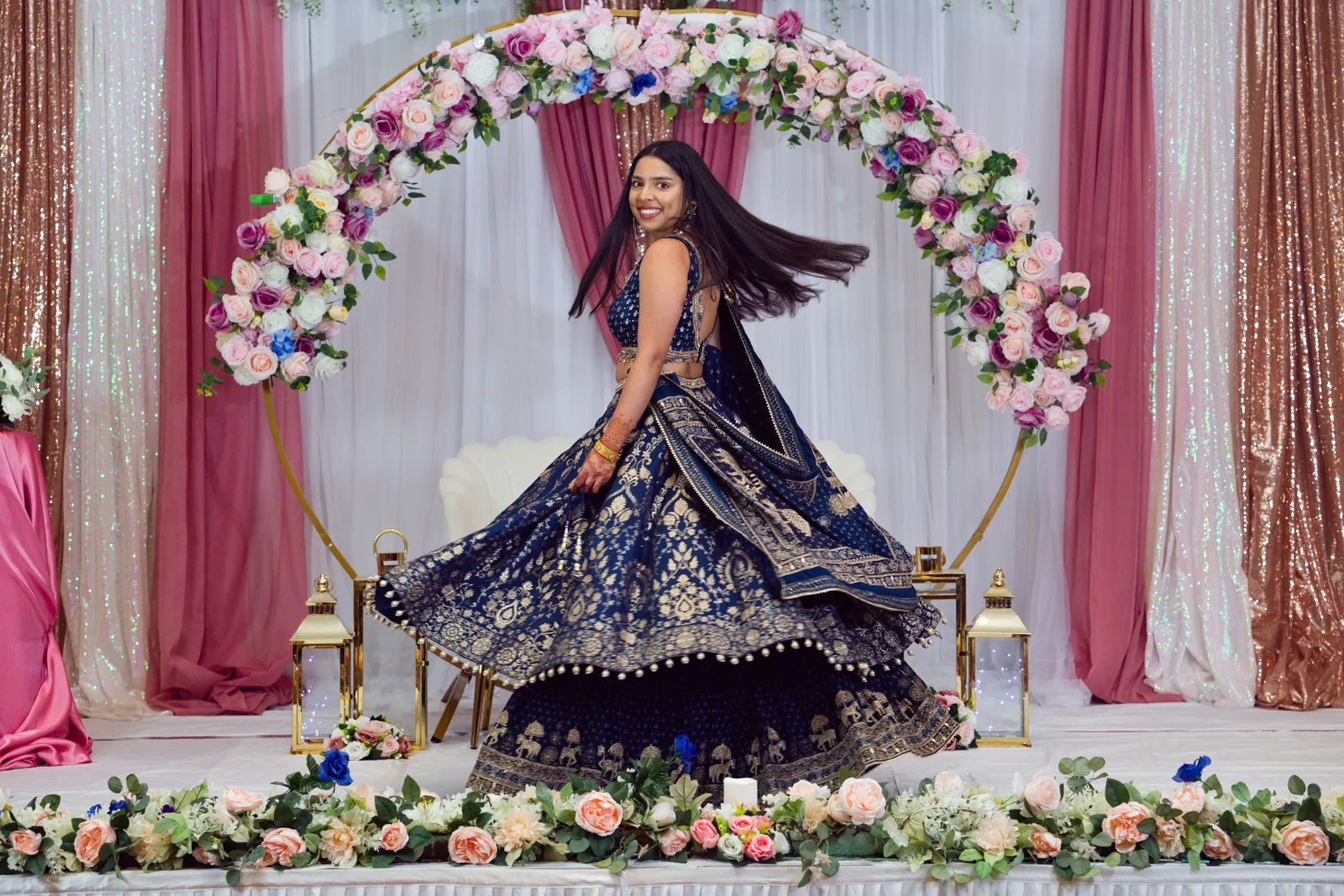 Indian bride twirling in a navy and gold lehenga in front of a floral arch at her wedding reception, Raleigh NC